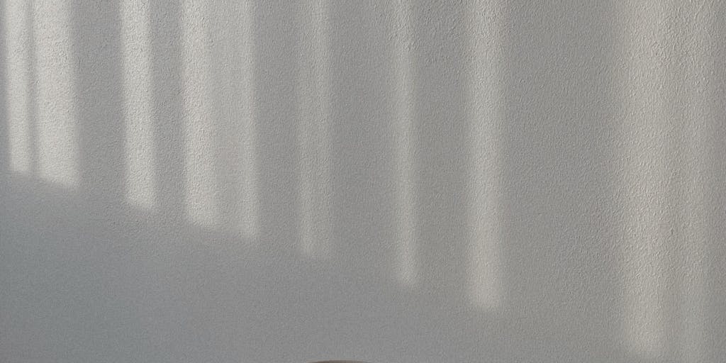 A close-up shot of a half-finished cup of tea or coffee, with a single, long, dramatic shadow cast by the cup and a nearby spoon. The background should be slightly blurred, perhaps showing a sunlit window or a stack of books, suggesting a moment of quiet contemplation during the afternoon. The lighting should be warm and golden, emphasizing the peaceful, reflective mood of the afternoon hours.