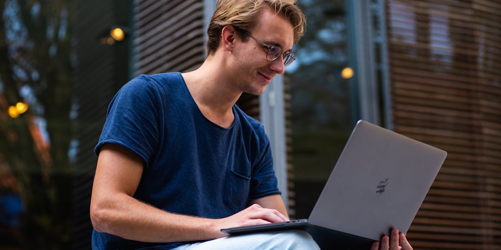 A close-up of a college student's hands typing on a laptop, with a visible screen showing a budgeting app and a section labeled 'Child Support'. Surrounding the laptop are college acceptance letters and a coffee mug, illustrating the blend of academic life and financial planning.