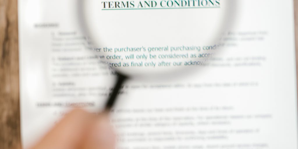 A close-up shot of a hand holding a magnifying glass over a contract filled with fine print, highlighting deceptive clauses. The background is blurred to emphasize the contract and the magnifying glass, symbolizing the need for scrutiny in legal documents.