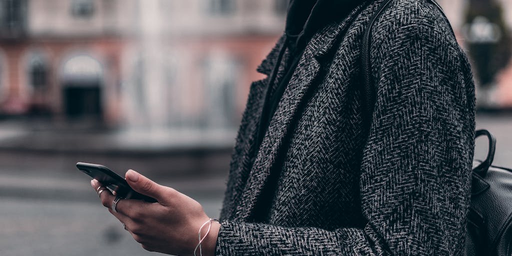 An artistic close-up of a smartphone screen displaying a Mutesix Review, with a hand holding the phone and a blurred cityscape in the background. This image conveys the idea of on-the-go access to reviews and modern technology.