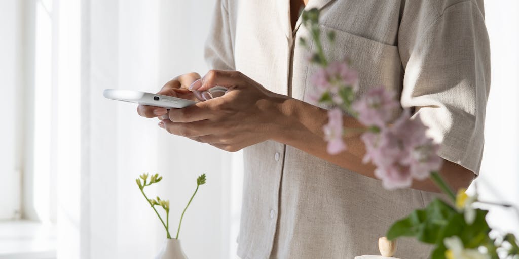 A close-up shot of a person’s hands typing on a laptop with Pinterest boards open on the screen. The background features a cozy coffee shop setting with plants and soft lighting, creating a warm and inviting atmosphere that reflects the lifestyle of a Pinterest marketer.