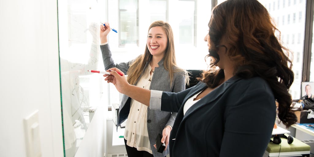 A team meeting in a modern conference room, with a whiteboard displaying a checklist of data room setup steps. The team members should be engaged in discussion, showcasing collaboration and strategic planning in setting up a data room.