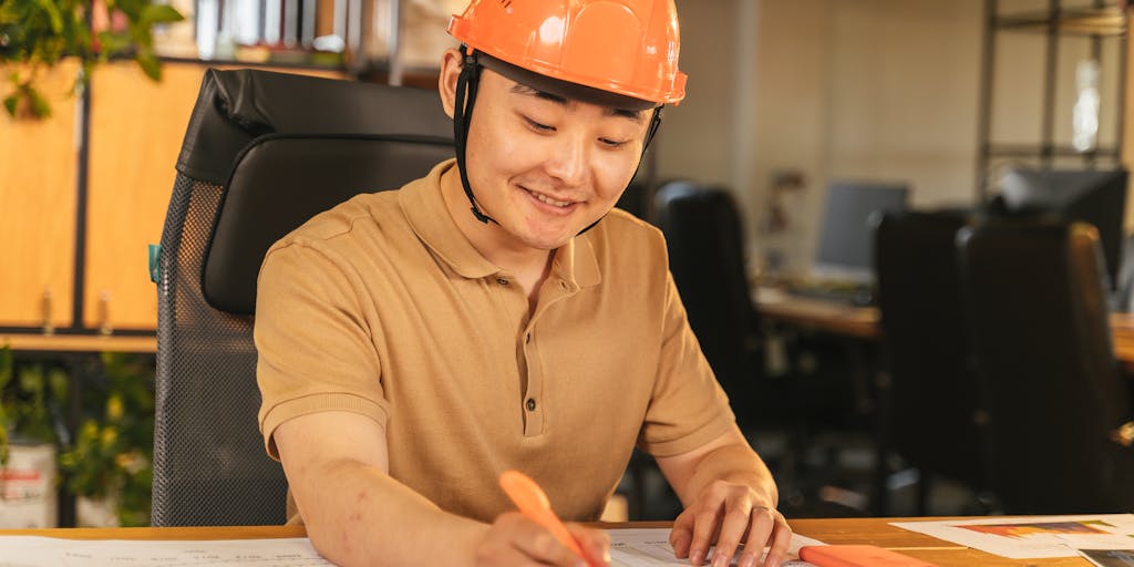 An image of a construction worker looking worried while holding a hard hat in one hand and a legal document in the other. The background features a blurred construction site, symbolizing the stress of an accident and the need for legal help.