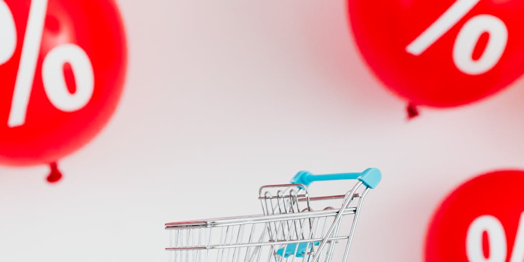 An artistic representation of a scale balancing two items: on one side, a shopping cart filled with discounted items labeled 'Sale', and on the other side, a person holding a 'For Sale' sign. This visual metaphor illustrates the balance between selling and sales.