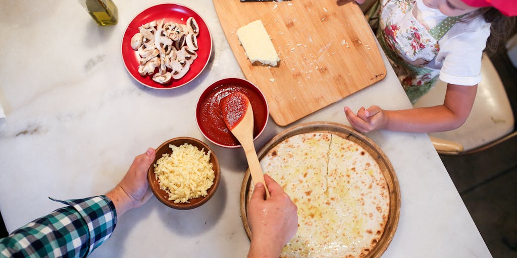 An overhead shot of a busy kitchen during meal prep, showcasing various ingredients laid out on the counter. A family member is chopping vegetables while another stirs a pot on the stove, illustrating the usual hustle and bustle of preparing dinner together.