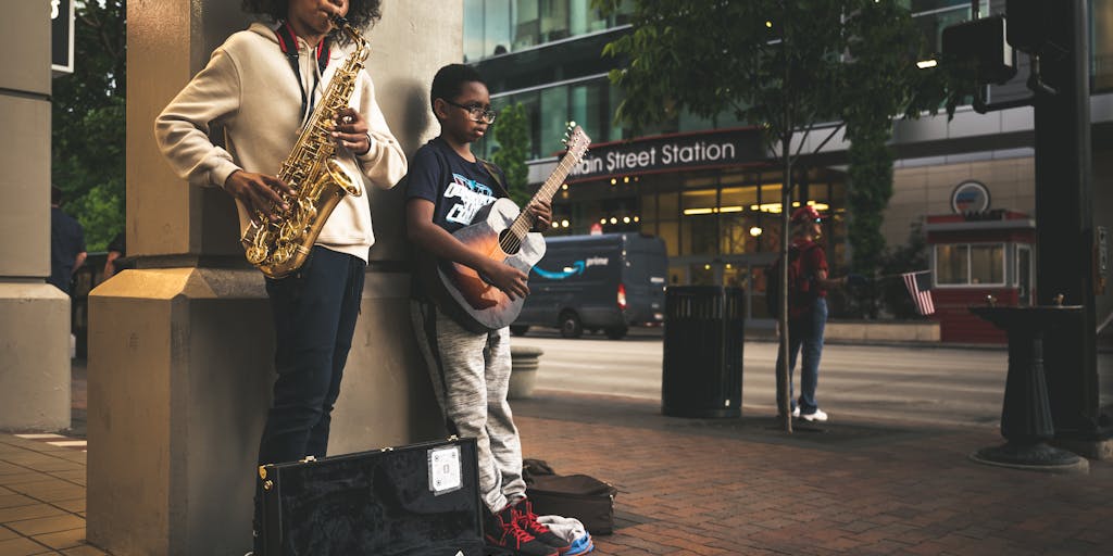 A whimsical scene of a street musician playing a guitar, with musical notes visually emanating from the instrument. The notes are creatively illustrated in the air, with the C note prominently featured, surrounded by vibrant colors.