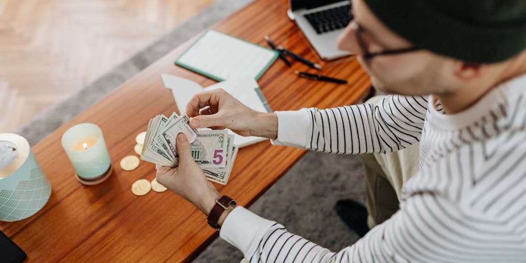 A close-up shot of a hand holding a stack of cash, with a serene background of a cozy home setting. The cash is neatly arranged, and soft natural light filters through a window, creating a warm and inviting atmosphere. This image symbolizes the comfort and security of settled finances.