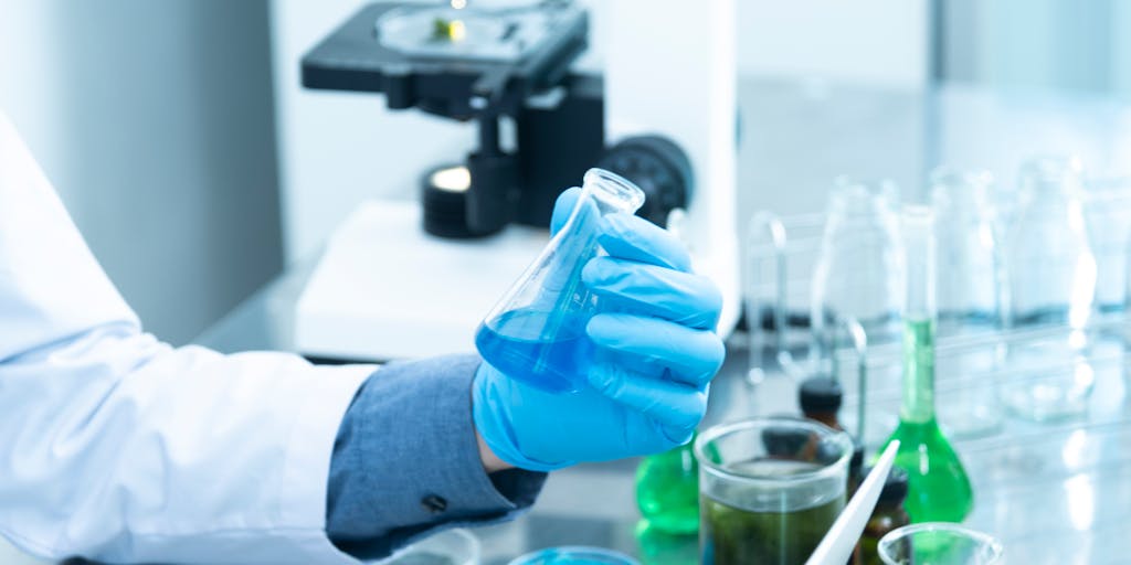 A research fellow in a modern laboratory, surrounded by high-tech equipment and scientific instruments. The fellow is intently examining a sample under a microscope, with notes and research papers scattered around. The image captures the essence of focused research and innovation.