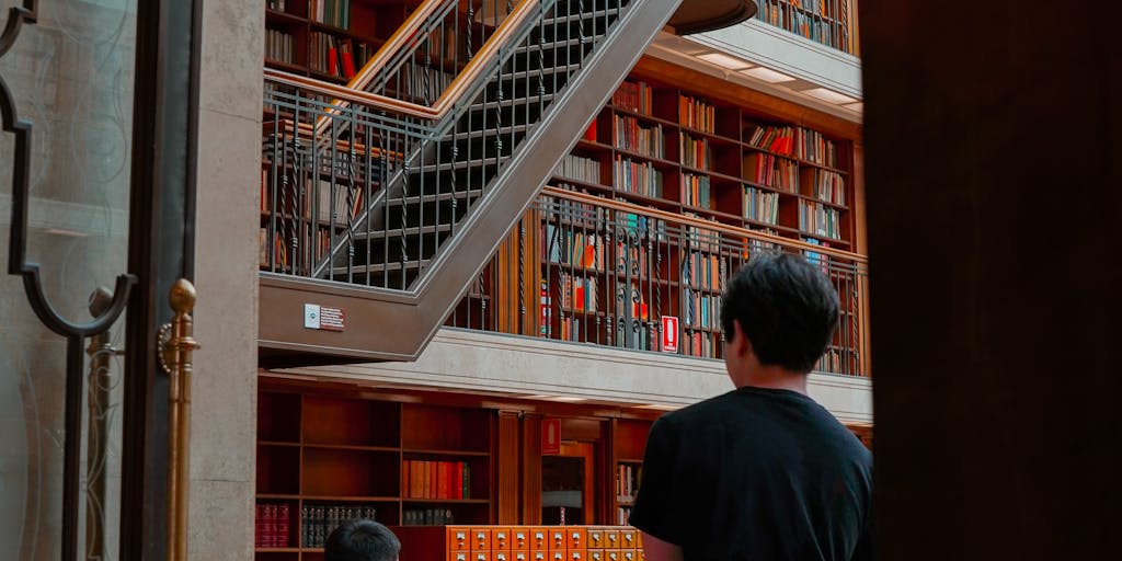 A candid shot of a research fellow working in a cozy library or study, surrounded by stacks of books and papers. The fellow is deep in thought, writing notes in a notebook, with a cup of coffee nearby. This image conveys the intellectual and solitary aspects of research.