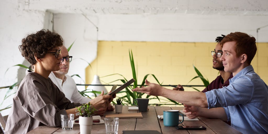 A group of diverse research fellows collaborating on a project in a bright, open workspace. They are gathered around a table filled with laptops, charts, and coffee cups, discussing ideas and brainstorming. This photo emphasizes teamwork and the collaborative nature of research.