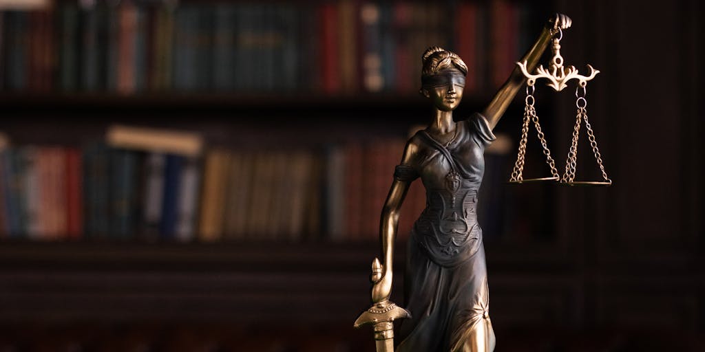 An artistic close-up of a gavel resting on a stack of legal books, with a luxurious pen and a contract in the background. The lighting highlights the textures and conveys the seriousness and prestige of high-stakes legal work.