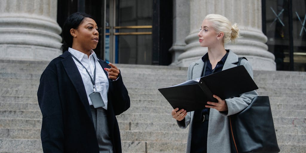 A group of diverse, high-powered attorneys in tailored suits standing confidently outside a historic Maryland courthouse. They are engaged in a lively discussion, with one holding a briefcase and another pointing towards the building, showcasing teamwork and leadership in the legal field.