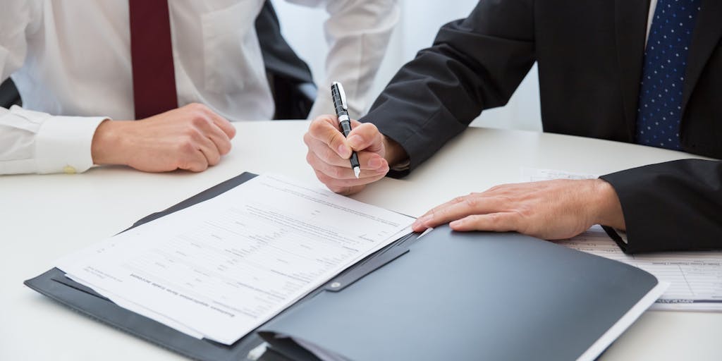 An artistic shot of a lawyer's hand holding a pen poised over a contract, with a blurred background of a high-rise building in Maryland. The focus on the pen symbolizes the power of negotiation and the importance of contracts in the legal profession, highlighting the financial success of top lawyers.