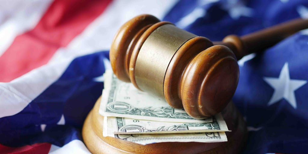 An artistic shot of a gavel resting on a stack of money, with a blurred background of a courtroom. This image represents the financial success and high stakes involved in the legal profession, particularly for the highest paid lawyers.