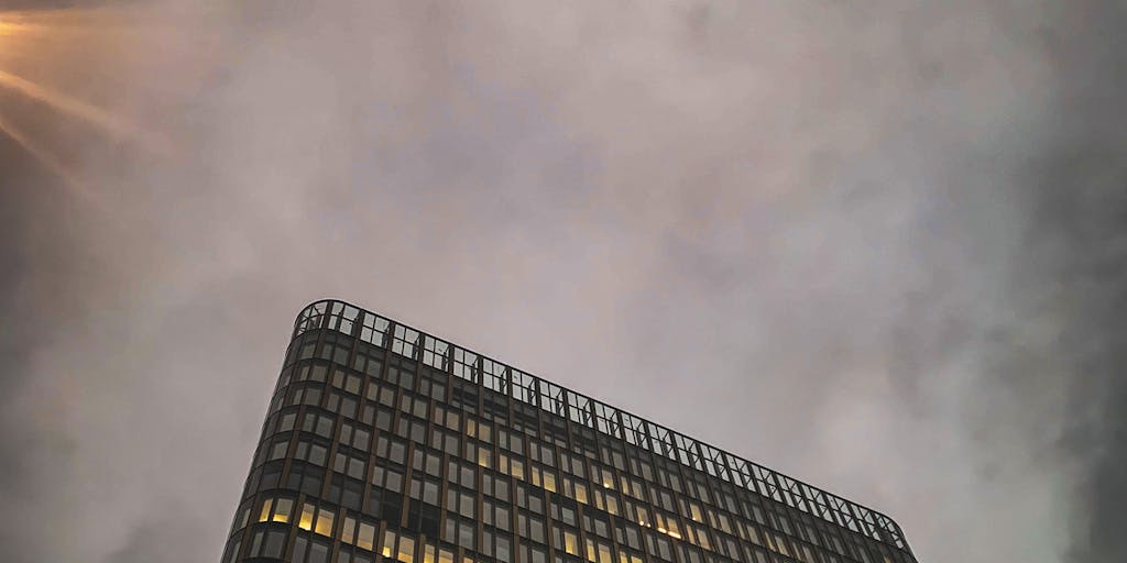 A dramatic shot of a high-rise office building in Vienna, with a sleek, modern design, symbolizing the prestigious law firms where the highest paid lawyers work. The image should capture the building at sunset, with warm light reflecting off the glass facade, conveying a sense of success and ambition.