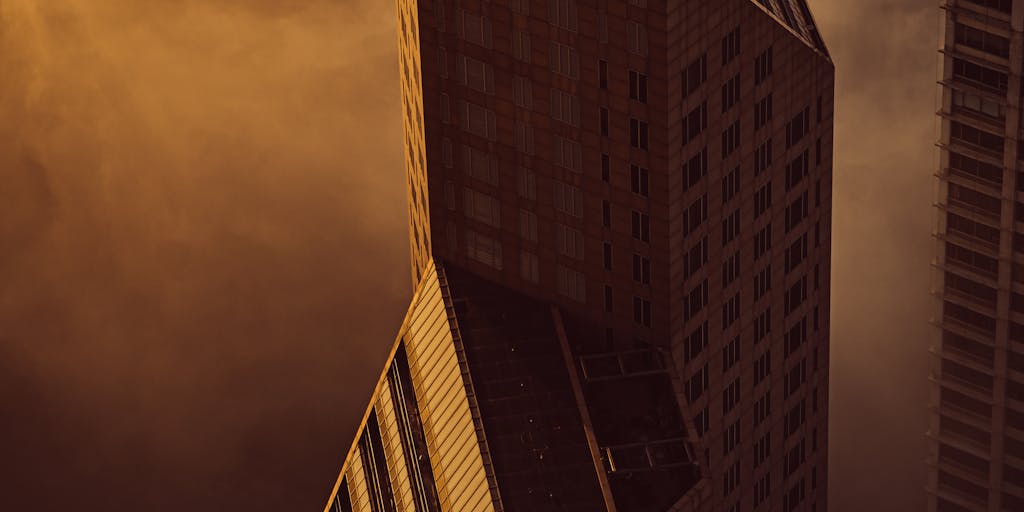 A dramatic shot of a high-rise office building in Bahrain, symbolizing the prestigious law firms where the highest paid lawyers work. The image should capture the building at sunset, with the warm glow reflecting off the glass, and a silhouette of a lawyer in a suit looking out from a window, representing ambition and success.