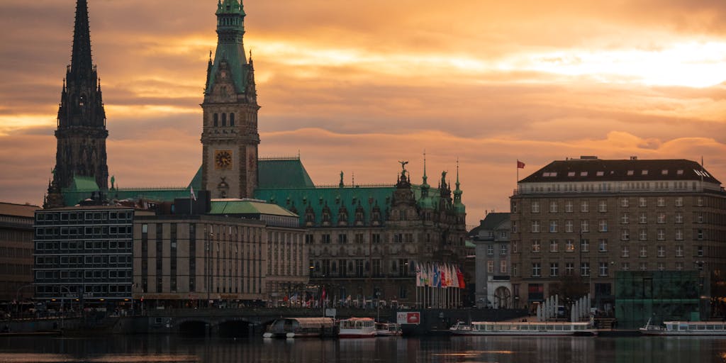 A dramatic shot of a high-rise office building in Helsinki, with a sleek, modern design, symbolizing the prestigious law firms where the highest paid lawyers work. The image should capture the building during sunset, with warm light reflecting off the glass, creating a sense of success and ambition.