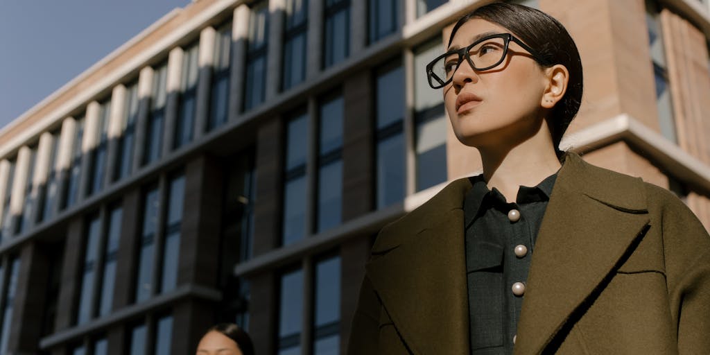 A dramatic shot of a high-rise office building in Milan, with a sleek, modern design. The building's glass facade reflects the skyline, symbolizing the success and prestige of the highest paid lawyers in Italy. In the foreground, a well-dressed lawyer is seen walking confidently towards the entrance, briefcase in hand, embodying ambition and professionalism.