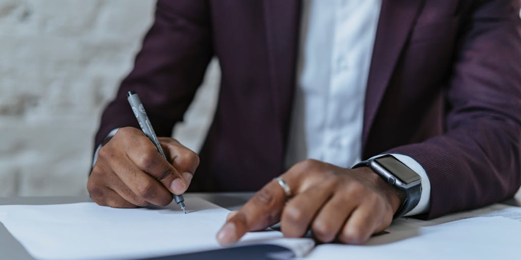 A close-up of a lawyer's hands as they sign a significant legal document, with a luxurious pen. The background features a blurred image of a prestigious law firm’s logo, emphasizing the importance of the moment. The focus on the hands and the pen symbolizes the power and responsibility that comes with being one of the highest paid lawyers.