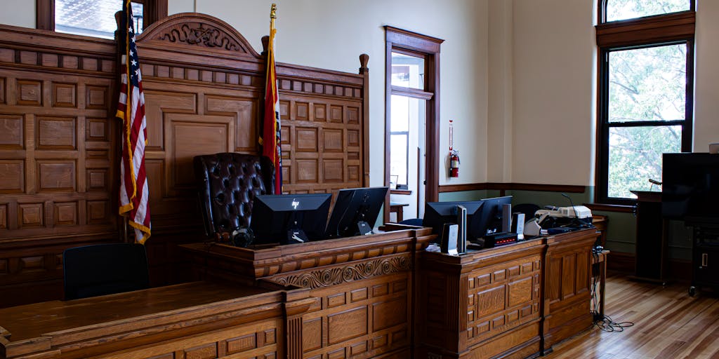 An artistic shot of a courtroom in North Korea, showcasing the unique architectural style of the building. The image captures the tension of a high-profile case, with the judge's gavel prominently in the foreground and blurred figures of lawyers and defendants in the background, highlighting the gravity of legal proceedings.