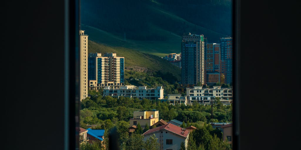 A dramatic portrait of a high-powered lawyer in a sleek, modern office overlooking Ulaanbaatar's skyline. The lawyer is dressed in an elegant suit, confidently reviewing legal documents on a glass desk, with a cityscape view in the background that symbolizes success and ambition.