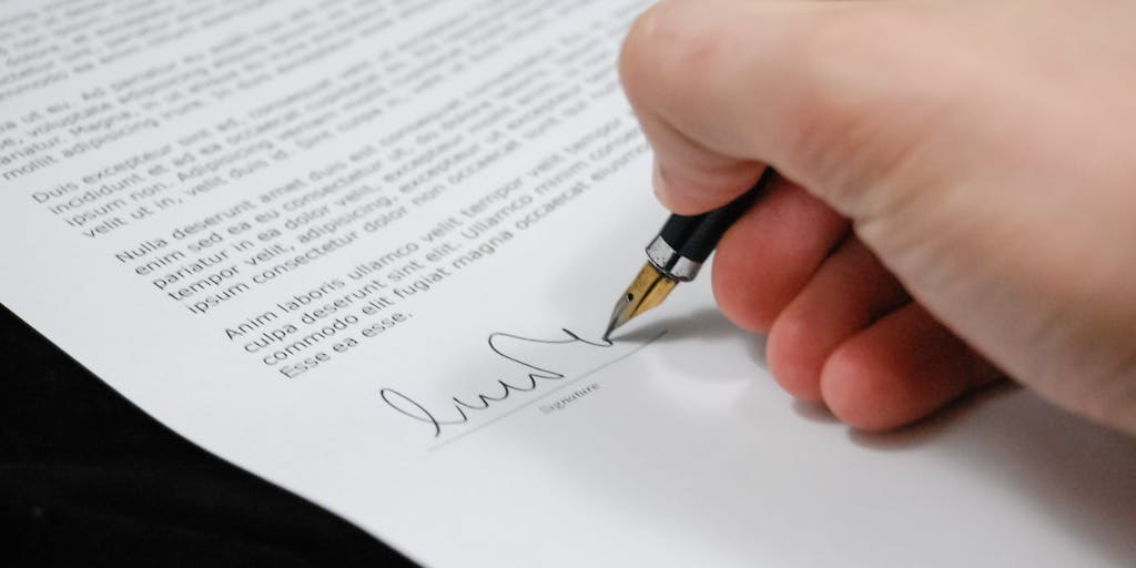 A close-up of a lawyer's hand holding a golden pen poised over a high-profile legal contract, with a blurred background of a modern law firm. The focus on the pen and contract highlights the importance of high-stakes legal work and the financial rewards that come with it.