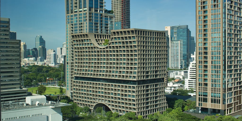 A dramatic shot of a high-rise office building in Bangkok, with a sleek, modern design, symbolizing the prestigious law firms where the highest paid lawyers work. The image should capture the skyline at sunset, with warm colors reflecting off the glass windows, creating a sense of ambition and success.