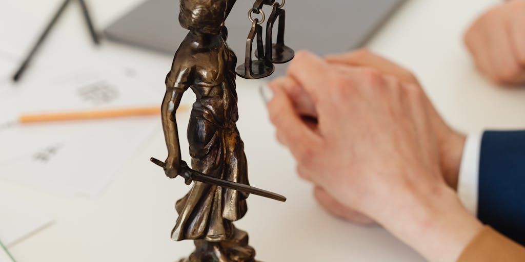 A close-up of a pair of hands in a tailored suit holding a golden gavel, with a blurred background of a prestigious law firm. The focus on the gavel represents authority and the high stakes involved in legal battles.