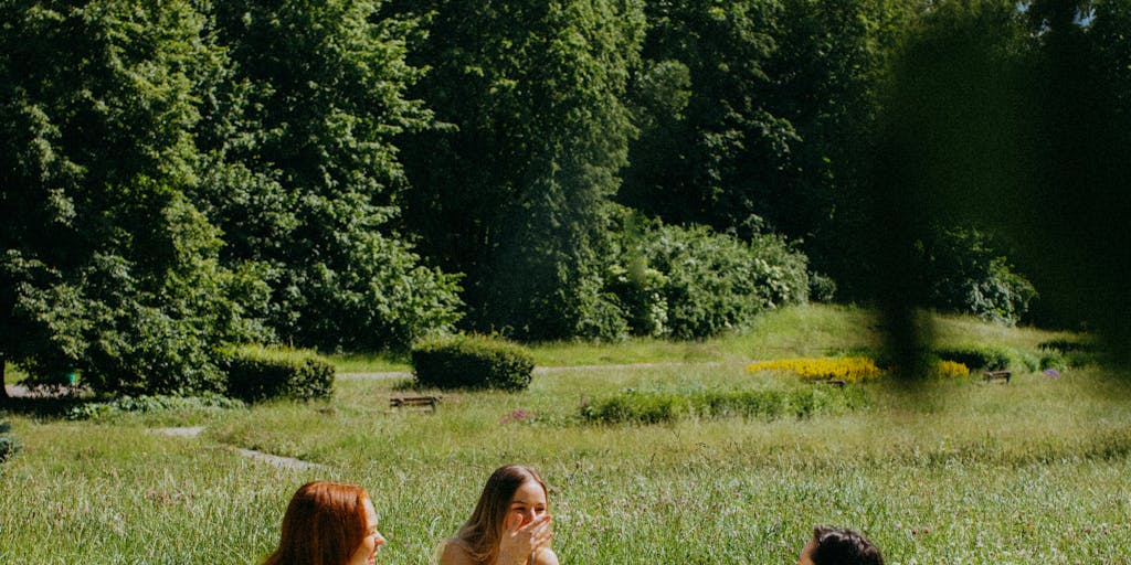 An outdoor picnic scene where friends are gathered around a picnic blanket, sharing a variety of colorful dishes. One person is playfully pretending to faint from the deliciousness of the food, while others react with laughter and surprise, capturing the essence of 'Oh My Lanta!'