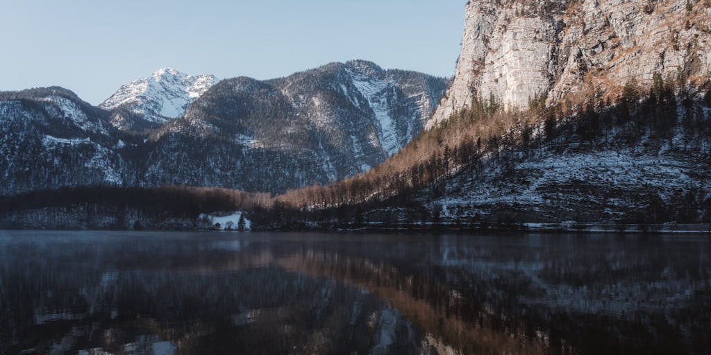 A serene landscape featuring a calm lake that perfectly reflects the surrounding mountains and trees. The photo captures the symmetry of nature, emphasizing the mirror image rule with a clear division between the real scene and its reflection in the water. The time of day is early morning, with soft light creating a magical atmosphere.