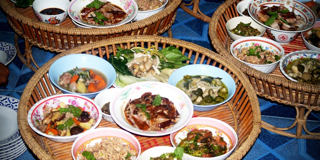 A close-up shot of a colorful buffet table filled with a variety of dishes from different cuisines, with labels that read 'Including But Not Limited To' next to each dish. The photo emphasizes the richness of cultural diversity in food.