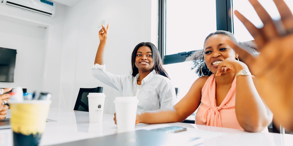 A group of diverse employees in a meeting room, looking attentively at a woman standing at the front, presenting with a confident posture. The room is filled with charts and graphs on a screen, illustrating the concept of apparent authority in a collaborative environment.