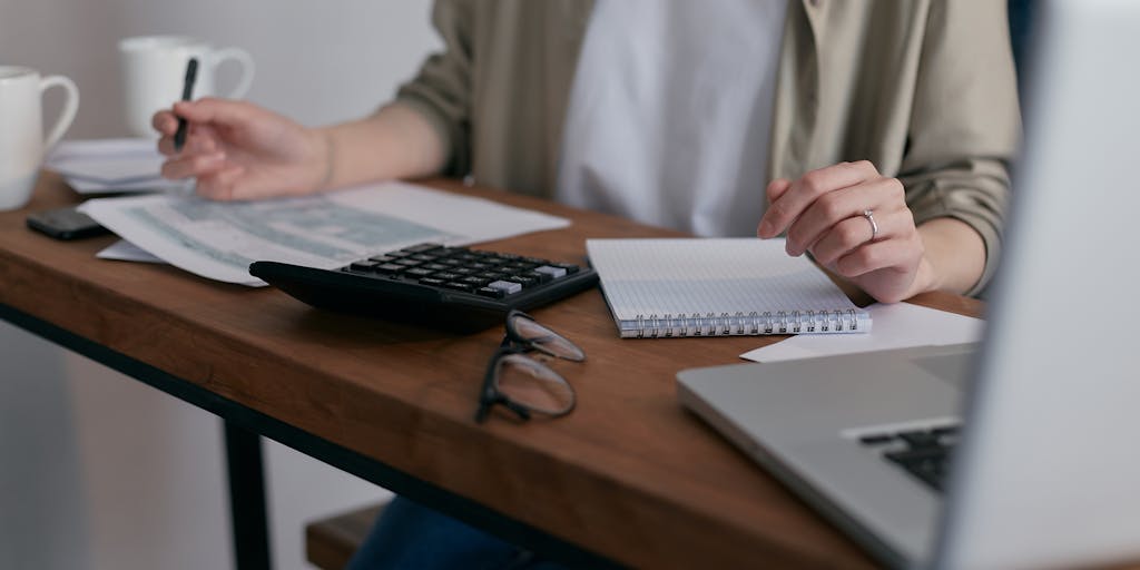 An image of a worried parent sitting at a kitchen table, surrounded by bills and a laptop displaying a child support calculator. The expression on their face should convey anxiety and concern about the financial implications of falling behind on payments.