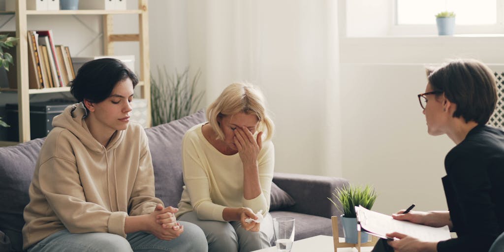 A conceptual photo of a parent sitting at a kitchen table with a laptop open, looking stressed while reviewing child support guidelines. The background features a calendar marked with important dates related to child support payments, illustrating the ongoing responsibilities and planning involved.