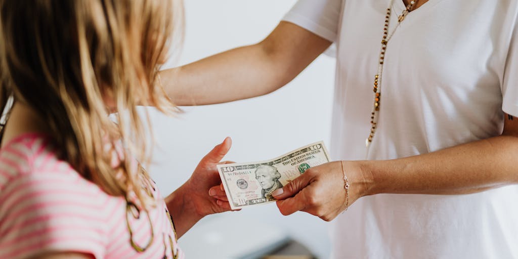 An artistic representation of a dollar bill morphing into a child's drawing, symbolizing the connection between financial support and children's well-being. The background features a faint outline of Trump's face, representing his influence on the topic.