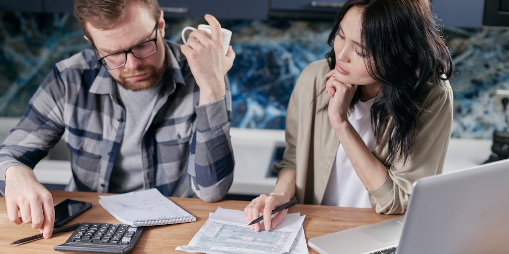 An overhead shot of a family sitting around a table with a laptop open, discussing finances. The table is cluttered with tax forms, a calculator, and a piggy bank, symbolizing the intersection of child support and financial planning.