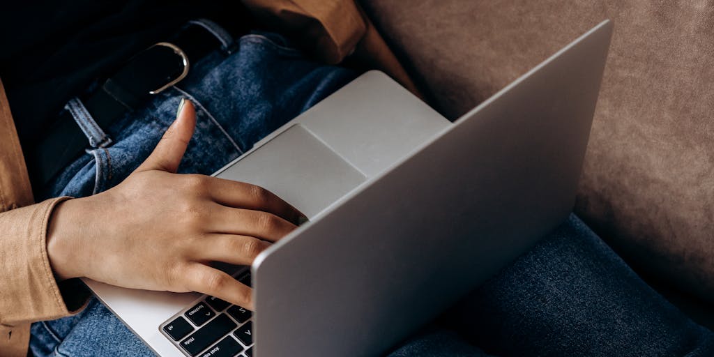 A close-up shot of a hand typing on a keyboard with the Systeme.io interface visible on the screen. The focus should be on the screen, showcasing a successful sales funnel or email campaign, with a blurred background of a cozy home office setting.