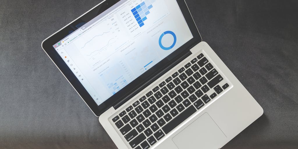A close-up shot of a laptop screen displaying the Datanyze dashboard, with colorful graphs and analytics visible. In the foreground, a person is taking notes on a notepad, symbolizing the process of analyzing data. The background is softly blurred to keep the focus on the screen and the note-taking.
