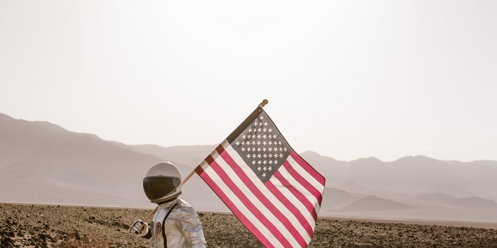 An artistic representation of the Apollo moon landing, featuring a silhouette of an astronaut planting a flag on a lunar surface made of sand. The background is a starry night sky, with a large, glowing moon illuminating the scene.