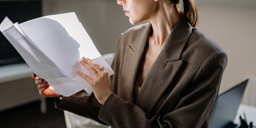 A close-up shot of a person sitting at a desk, intently reviewing emails on a laptop screen. The screen displays the Reachinbox interface, with colorful graphs and metrics visible. The background is softly blurred to emphasize the focus on the screen, and a coffee cup sits nearby, suggesting a productive work environment.