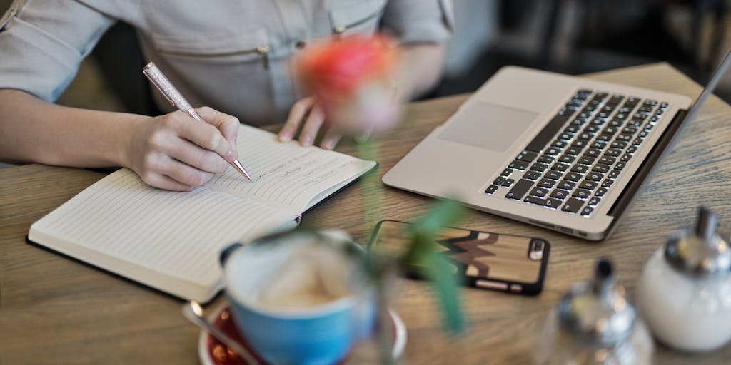 An overhead view of a desk with a laptop open to the Marketo Engage pricing page, alongside a notepad filled with handwritten notes and a cup of coffee. The scene captures a moment of contemplation and decision-making.