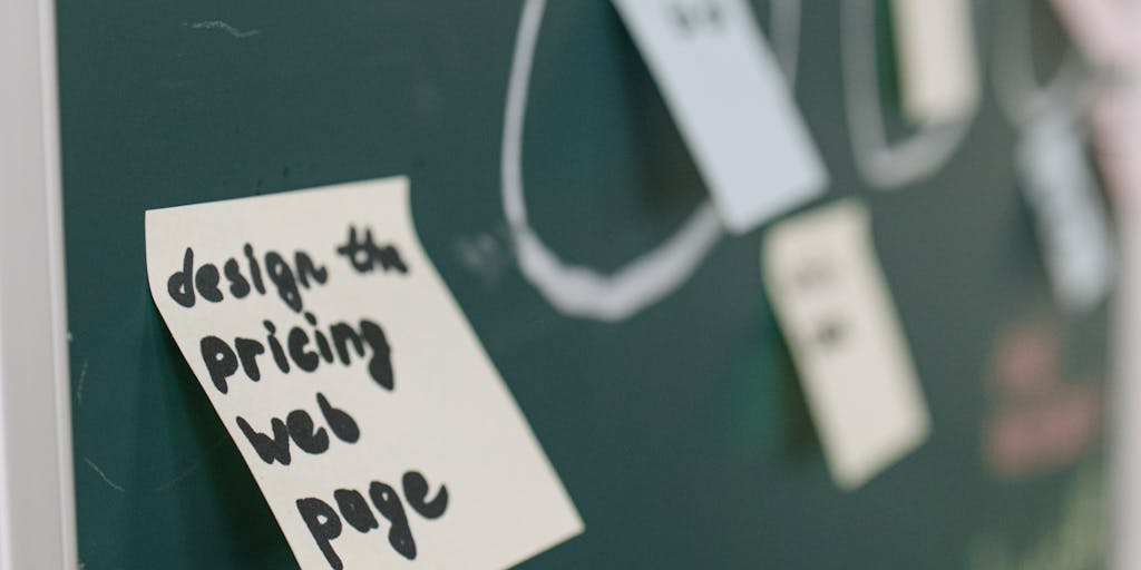 A close-up shot of a chalkboard with handwritten pricing tiers for a fictional service called 'Meetalfred'. The board is surrounded by colorful sticky notes and a cup of coffee, creating a cozy brainstorming atmosphere.