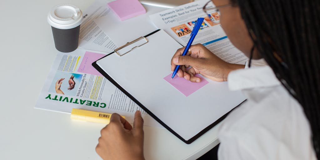 An overhead view of a workspace with a laptop open to the Yet Another Mail Merge pricing page, surrounded by colorful sticky notes and a calculator. The sticky notes contain handwritten reminders and pricing calculations, showcasing the planning process.