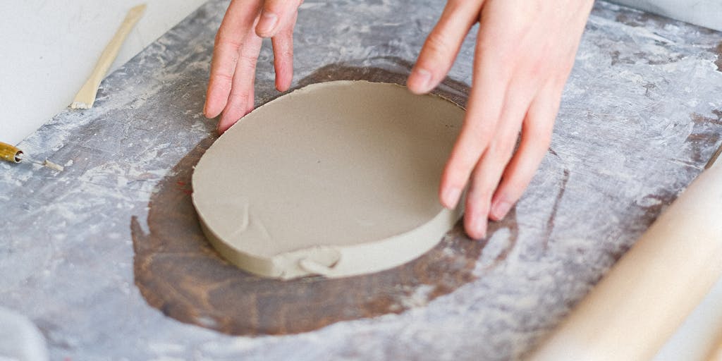 An overhead view of a creative pricing board made from clay, featuring different pricing options represented by colorful clay shapes (like circles or squares) with numbers on them. The board should be set on a wooden table with tools and materials for clay modeling around it, giving a vibrant and artistic feel.