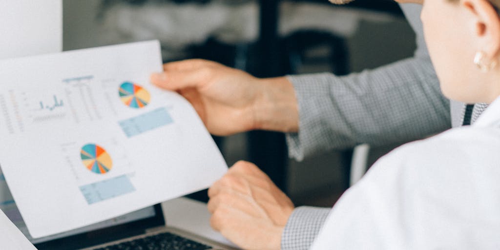 A group of diverse professionals gathered around a table, engaged in a lively discussion about Salesloft pricing, with a laptop open to a Reddit page. The atmosphere is collaborative, showcasing the importance of community feedback in making informed purchasing decisions.
