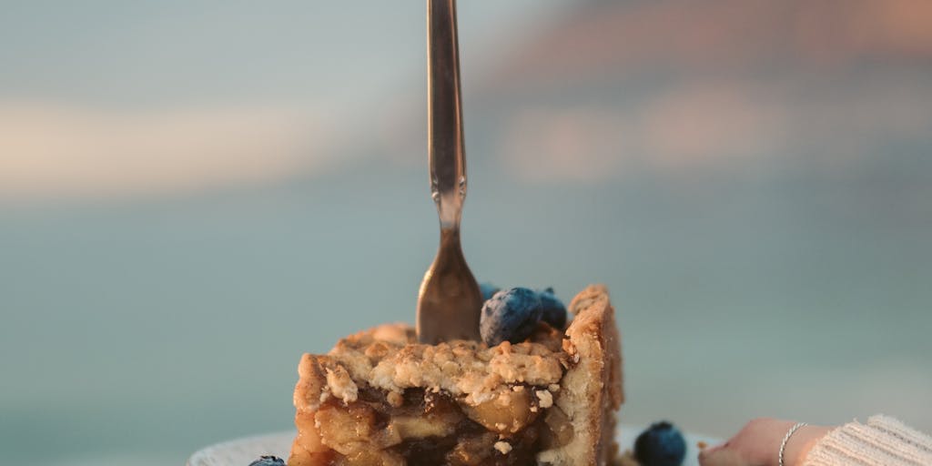 A close-up shot of a hand holding a slice of pie with a price tag attached to it, symbolizing the concept of pricing. The background features a blurred image of a digital screen displaying Piesync's pricing plans, merging the physical and digital worlds.