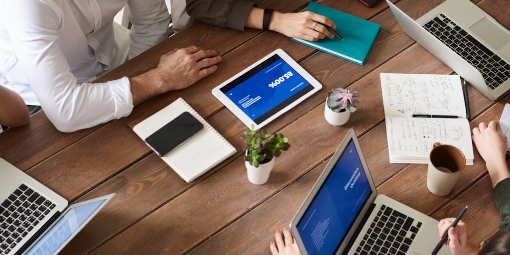 A group of diverse individuals sitting around a table, engaged in a discussion about Voy Media Reviews. Capture their expressions of excitement and curiosity, with laptops and tablets open in front of them, showcasing a collaborative atmosphere.