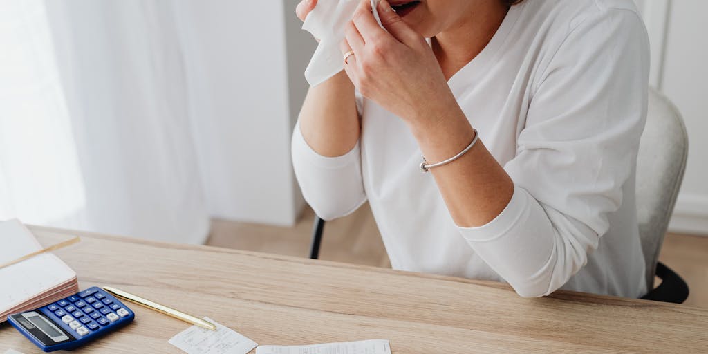 A close-up shot of a person holding a stack of unpaid bills and a calculator, looking contemplative. The background features a blurred image of a child playing, symbolizing the connection between finances and parenting responsibilities.