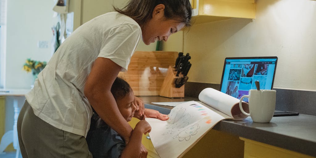 An image of a parent sitting at a kitchen table with a laptop open, looking contemplative while reviewing child support termination forms. The scene is warm and inviting, with a child’s drawing on the fridge in the background.