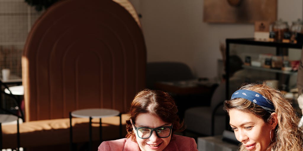 A candid moment captured in a coffee shop where two parents are discussing their joint custody arrangement over coffee, with documents and a laptop open in front of them. The atmosphere is friendly, showcasing collaboration and communication in co-parenting.